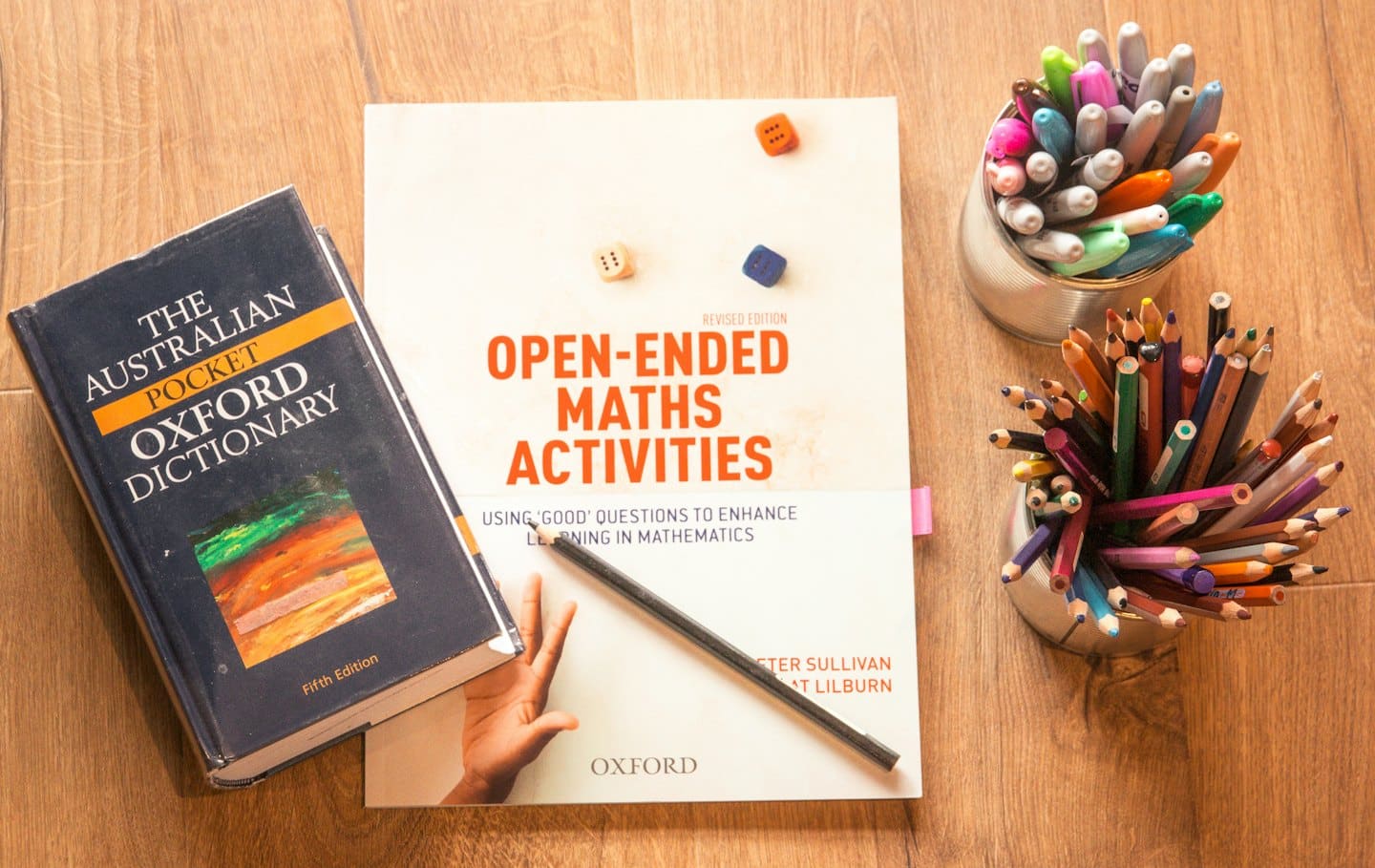Maths textbook and dictionary with colorful pens and dice.