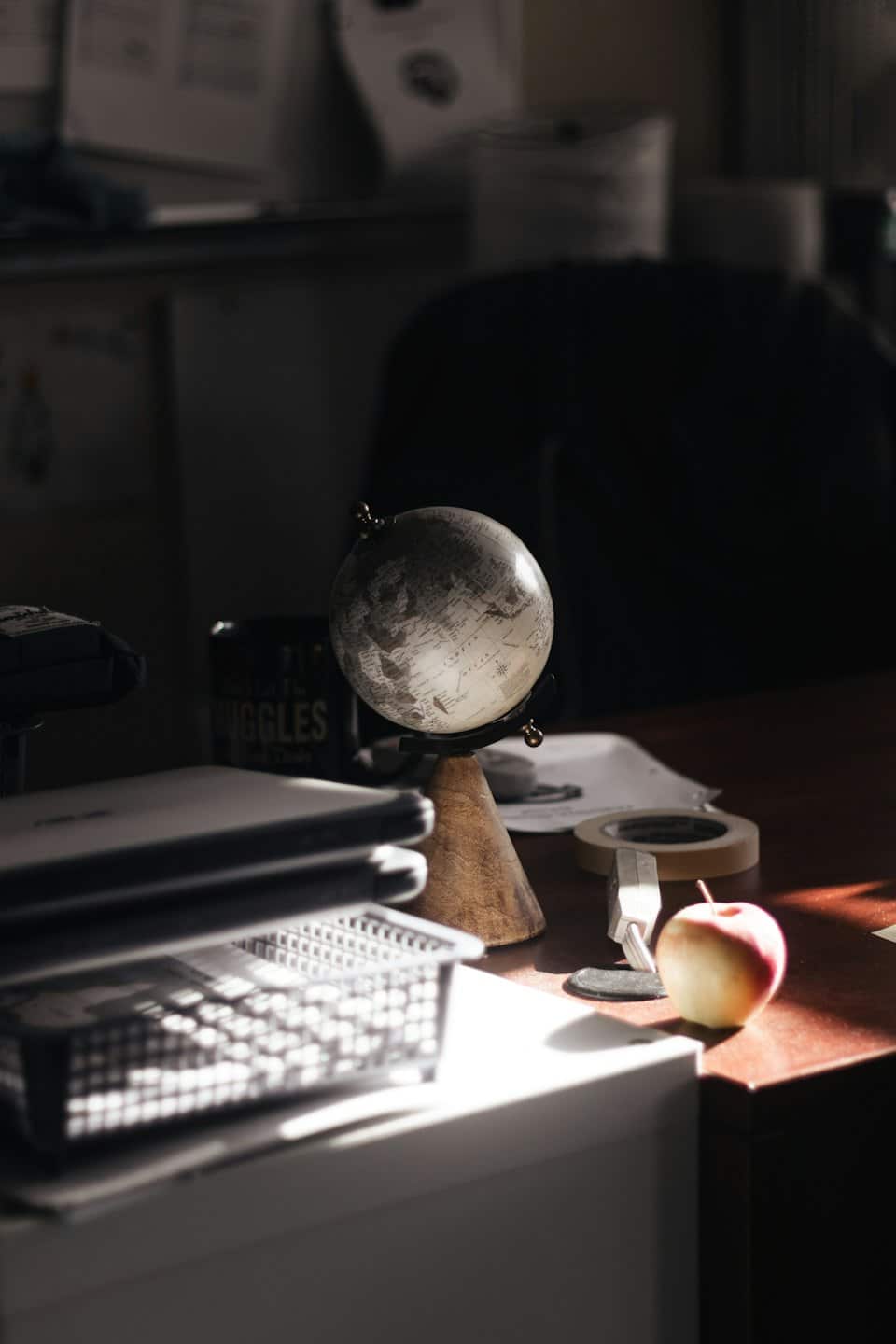 A desktop globe rests on a wooden desk next to a laptop and documents.