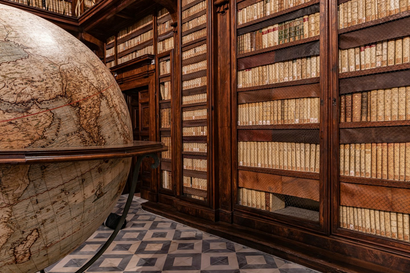 An antique globe stands before bookshelves in an old library.